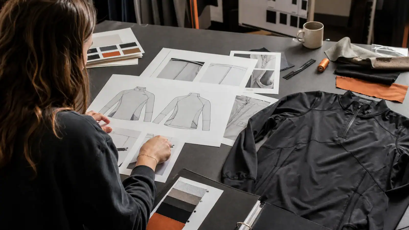 AI-generated illustrative apparel designer reviewing garment flats, construction details and fabric swatches