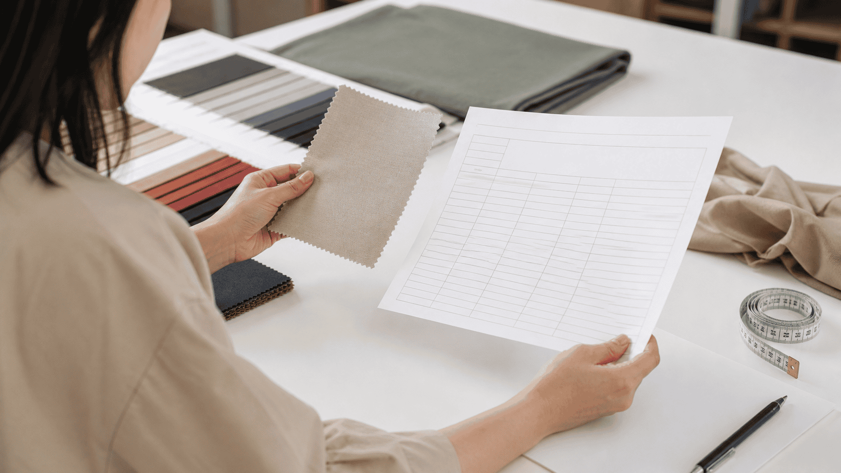 Apparel developer reviewing a fabric swatch and blank measurement sheet at a design table