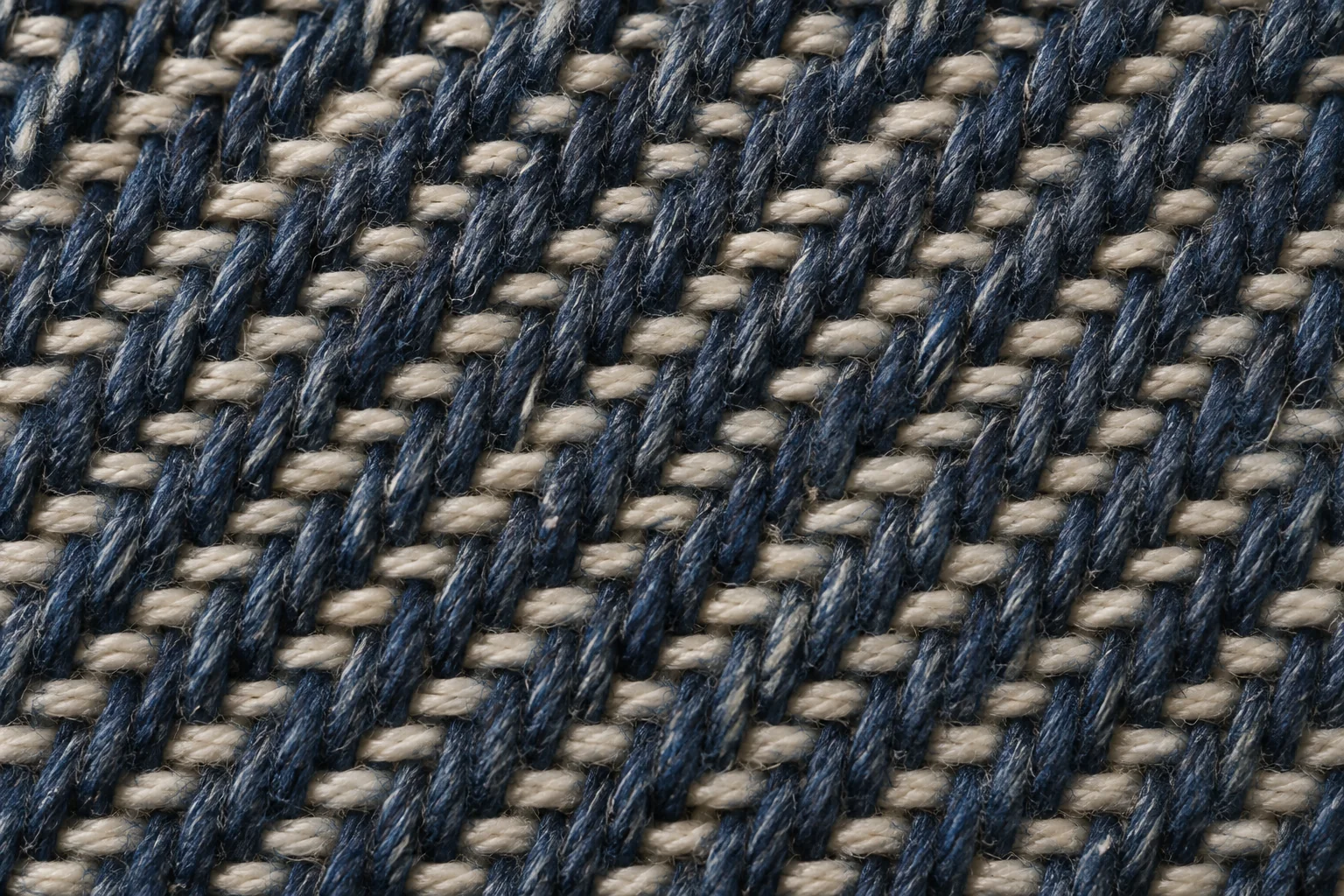 Macro study of denim showing indigo warp yarns crossing lighter filling yarns and forming a diagonal twill line under side lighting, no text